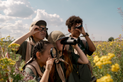 four kids in the grass looking through binaculars