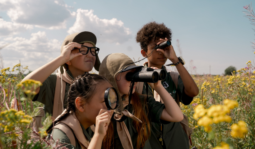 four kids in the grass looking through binaculars